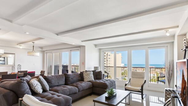 Un salon spacieux avec un grand canapé d’angle, un coin repas et un balcon offrant une vue sur la mer.