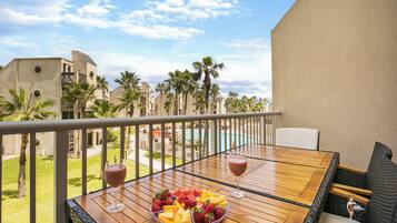 A balcony with a wooden table, two glasses of red beverage, and a fruit bowl.