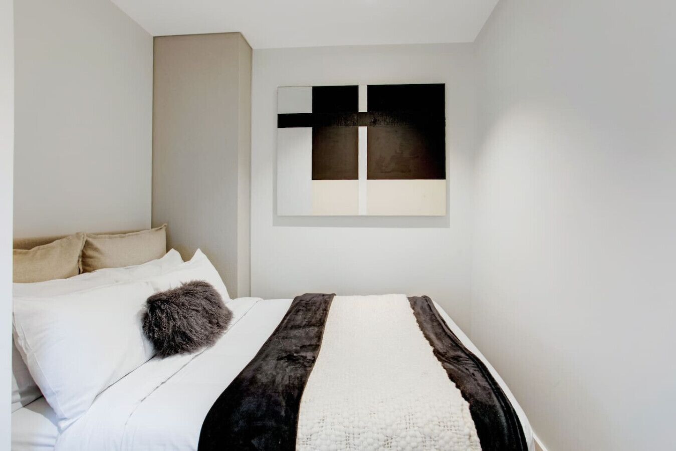 Une chambre à coucher avec un lit, des oreillers et une œuvre d’art accrochée au mur.