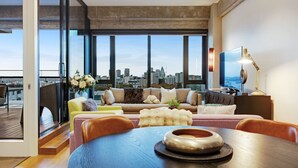 A modern living room with a city view, featuring a sofa, chairs, a coffee table, and a TV. - Premium Cityscape Abode w Skytower view & Parking (Auckland CBD)