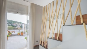 A modern interior with a staircase, a view of a balcony with outdoor seating, and a cityscape in the background. - Le Cavottole Resort (Vico Equense)
