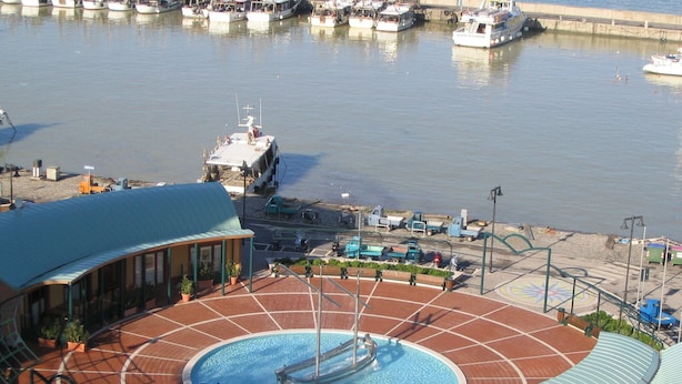 A swimming pool with a fountain, surrounded by a tiled deck and a covered area with benches.