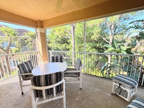 A covered outdoor seating area with a table and chairs, a railing, and a view of greenery and buildings.
