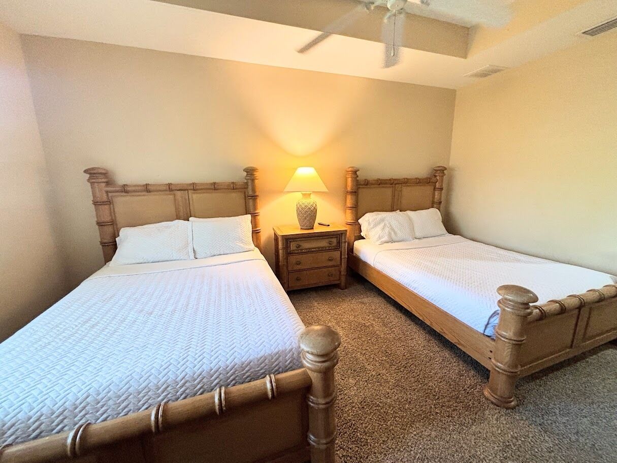 A bedroom with two single beds, a nightstand with a lamp, and a ceiling fan.