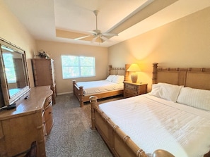 A bedroom with two beds, a ceiling fan, a dresser, and a window with blinds.