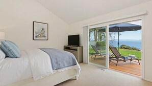 Quarto com cama, televisão, pintura e varanda vista para o mar.