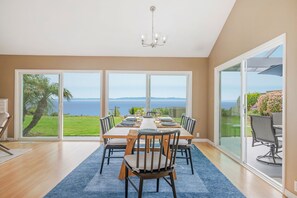 A dining area with a view of the sea, a chandelier, and a large sliding glass door. - Oceanfront Sanctuary | Endless Horizons, Private Hot Tub, Walk to Beach & Parks (Santa Barbara)
