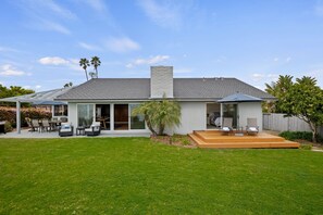 A modern house with a spacious backyard, a patio with outdoor furniture, and a large sliding glass door leading to a covered patio area. - Oceanfront Sanctuary | Endless Horizons, Private Hot Tub, Walk to Beach & Parks (Santa Barbara)
