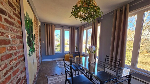 A dining area with a glass table, black chairs, and a vase with flowers. - Under the Sun Apartment (Boston)
