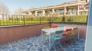 An outdoor patio with a stone floor and a white table surrounded by colorful chairs.