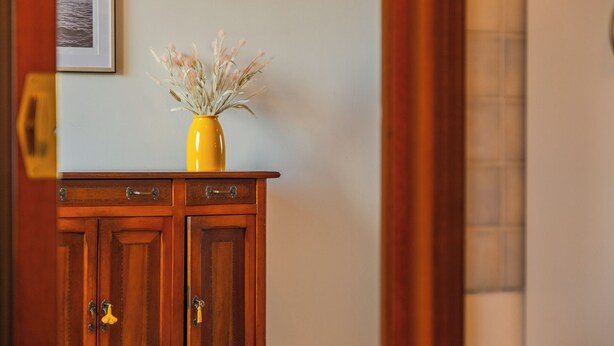 A wooden cabinet with a yellow vase containing dried flowers.