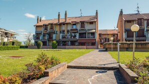A multi-story residential building with balconies, a paved pathway, and a well-maintained garden.