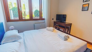 A hotel room with a large bed, a television on a wooden table, and a window with a view of greenery.