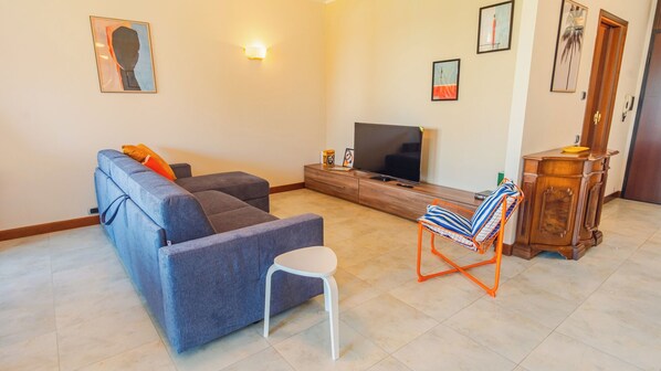 A living room with a sofa, a TV, a small white chair, and a wooden cabinet. - Dimora dei Colori - Two Bedroom Apartment, Sleeps 6 (Sirmione)
