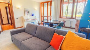 A living room with a grey sofa, a dining table with chairs, and a piano.