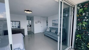 Un salon moderne avec un canapé, un lit et une porte-fenêtre coulissante donnant sur un balcon.