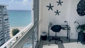Un balcon avec vue sur l’océan, un bureau avec une chaise, une poubelle et des étoiles de mer décoratives accrochées au mur.