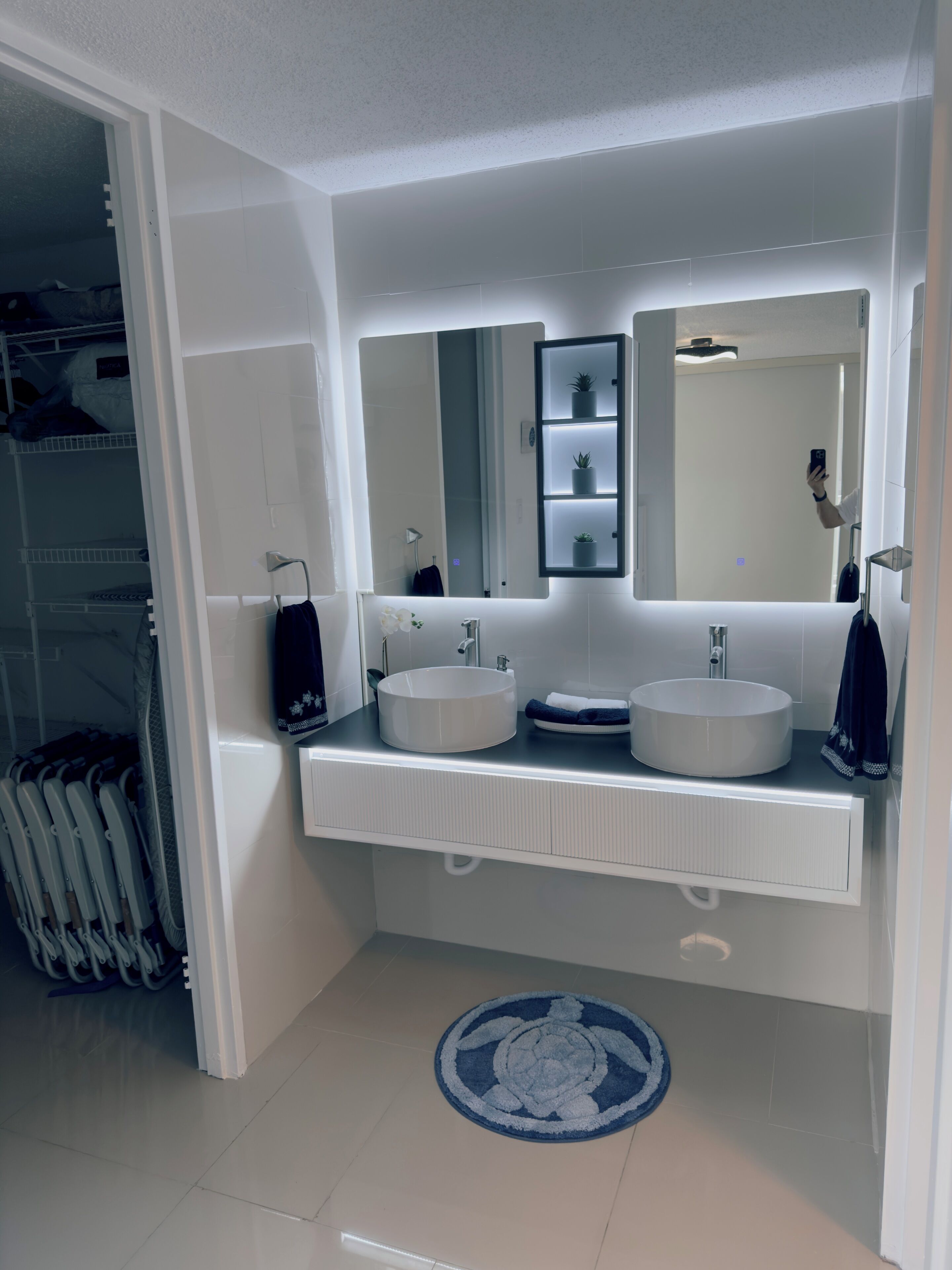 Un baño moderno con dos lavamanos, un espejo grande y un estante empotrado con plantas.