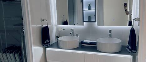 Un baño moderno con dos lavamanos, un espejo grande y un estante empotrado con plantas.
