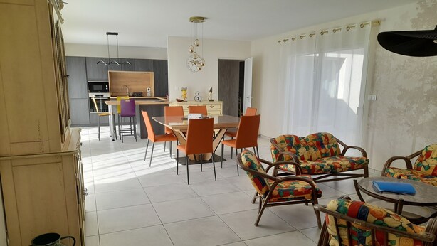 Ruime eethoek met oranje stoelen en een tafel, een keuken op de achtergrond, en een decoratieve wandklok.