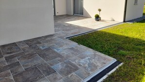 Een modern gebouw met een betegeld terras, een klein gazon en een plant in een pot.