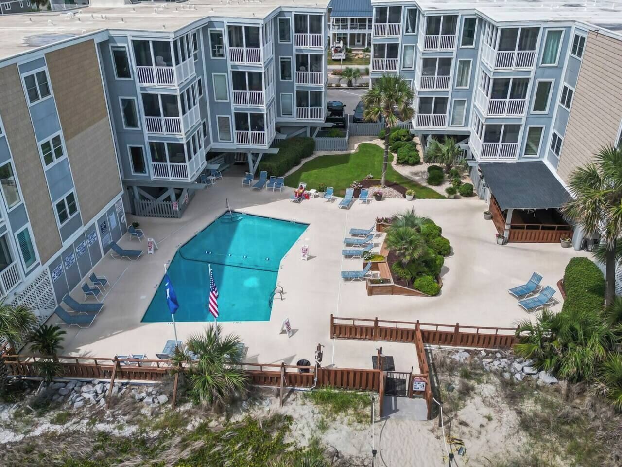 A multi-story building with a swimming pool surrounded by lounge chairs and a small garden area.