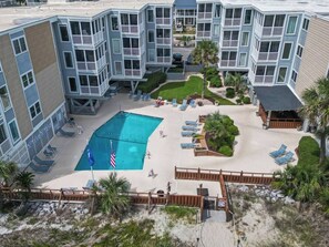 A multi-story building with a swimming pool surrounded by lounge chairs and a small garden area.