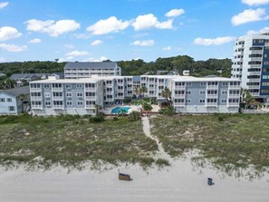 Un hotel frente a la playa con edificios de varios pisos, piscina y una playa de arena.