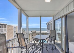 A balcony with a table and chairs, overlooking a beach and ocean.