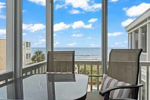 A balcony with a view of the ocean, two chairs, and a table.