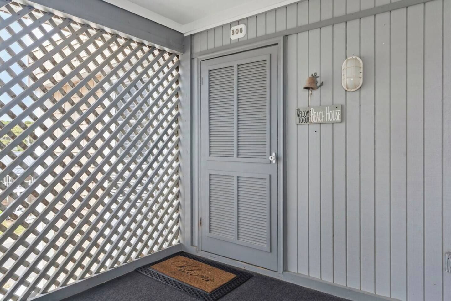 Una puerta gris con un letrero que dice 'Bienvenido a nuestra casa de playa' y el número '306' arriba.