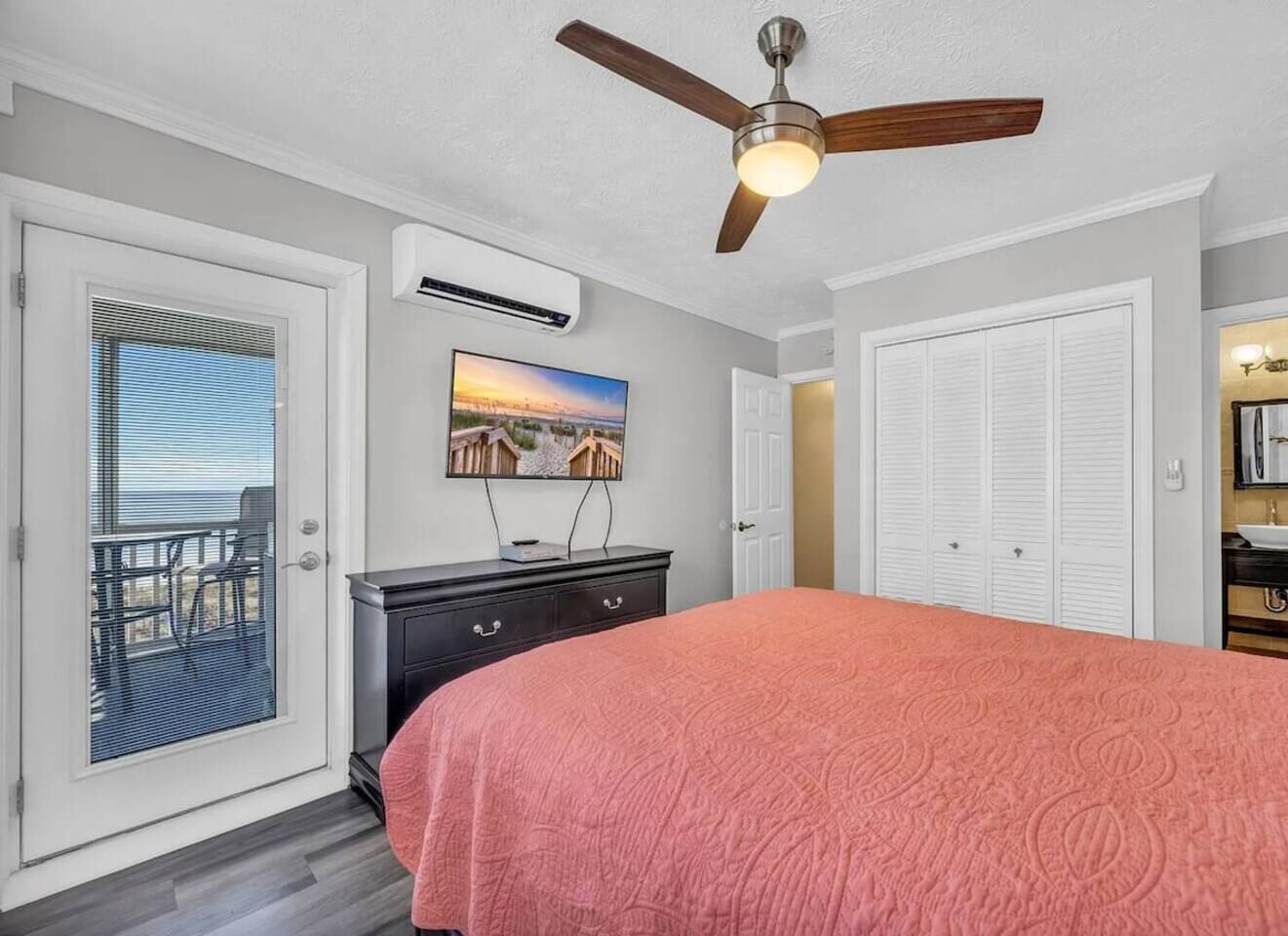 A bedroom with a bed, a ceiling fan, a TV, and a sliding door to a balcony.