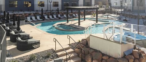 Un área de piscina con sillones reclinables, un pabellón y un pequeño jacuzzi.
