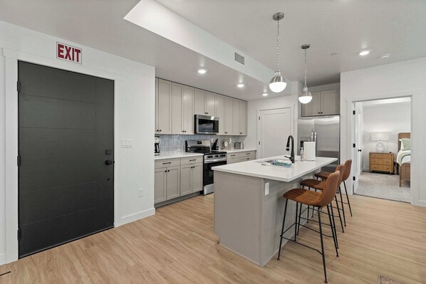 A modern kitchen with white cabinets, a large island with bar stools, a microwave, stove, and refrigerator. - Cliffside Vista Stay for 7! (Hurricane)