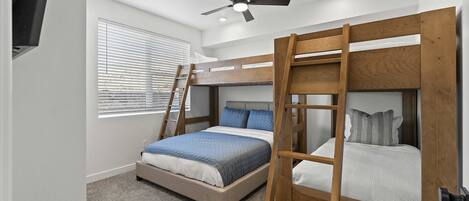 Un dormitorio con literas, ventilador de techo y ventana con persianas.