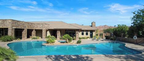 A house with a swimming pool, stone exterior, and a mountain backdrop.