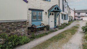 Un étroit sentier de gravier mène à une rangée de maisons traditionnelles aux murs de pierre et aux cadres de fenêtres bleus.