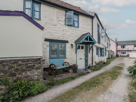 A narrow gravel path leading to a row of traditional cottages with stone walls and blue window frames.