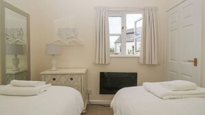 Une chambre avec deux lits, une commode, un miroir, une fenêtre avec des rideaux et une cheminée.