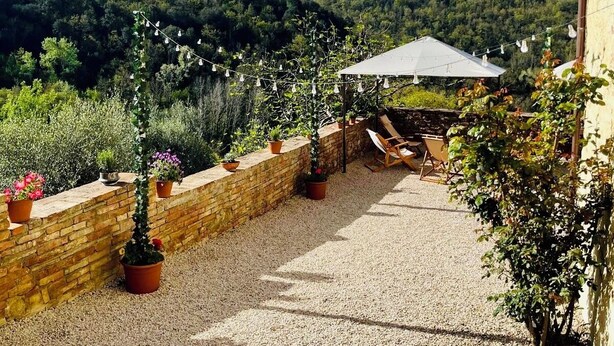 Un patio con piso de grava, plantas en macetas y un paraguas blanco.