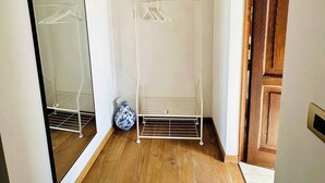 Una habitación con piso de madera, un armario metálico blanco, un espejo y una puerta de madera.