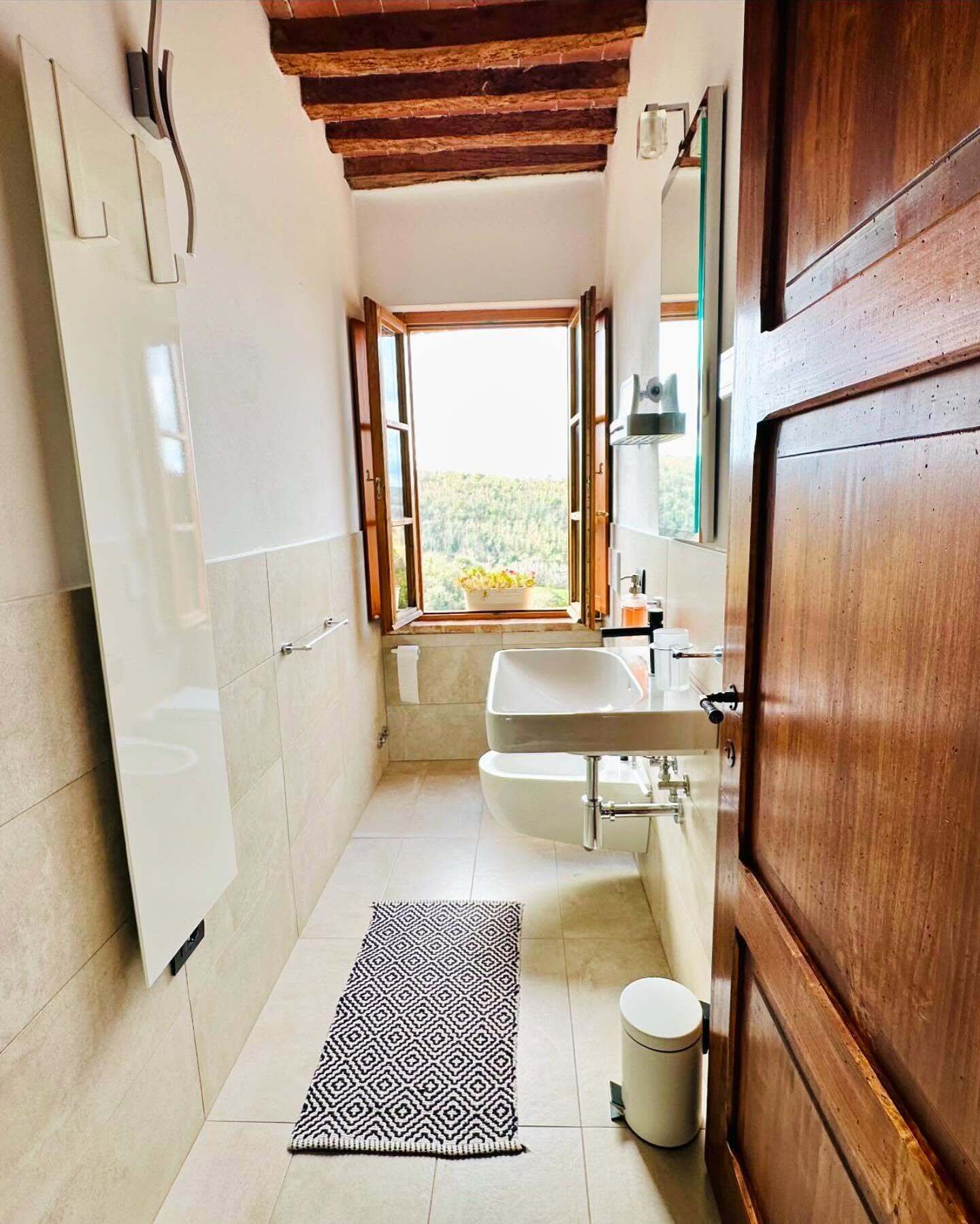 A narrow bathroom with a window, a sink, and a toilet.