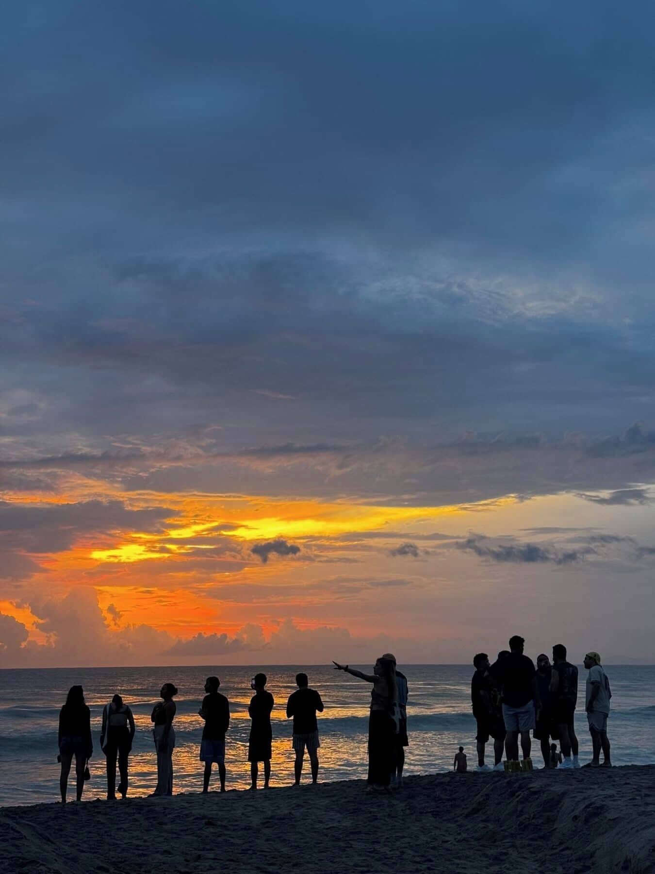 A beach scene with people silhouetted against a sunset.