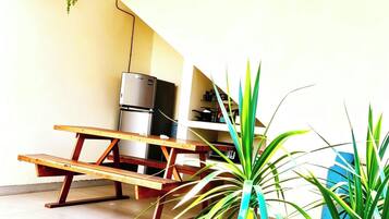 Un patio techado con ventilador de techo, un refrigerador y una mesa de madera.