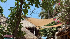 A narrow street with thatched-roof buildings, a signpost with directions to various local attractions, and a sandy path leading towards the sea. - Casa PXM Ocean view (Puerto Escondido)