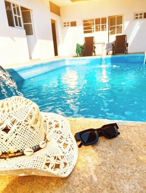 Zona de piscina con un sombrero blanco de ganchillo, gafas de sol y una silla.