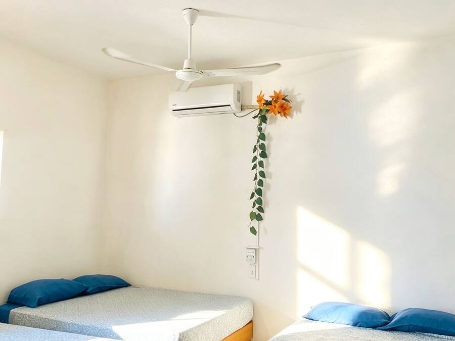 Quarto com duas camas, ventilador de teto, ar condicionado e tomada na parede.