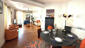 Un salon moderne comprenant un coin repas, un parquet et une grande fenêtre agrémentée de rideaux.