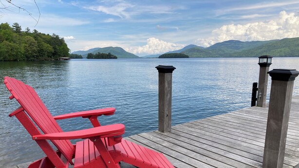 A red Adirondack chair on a wooden dock with a view of a lake and mountains in the background. - Fish Point Landing (Diamond Point)