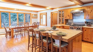 A spacious kitchen with wooden cabinets, a large island, and a dining area with chairs and a table. - Fish Point Landing (Diamond Point)